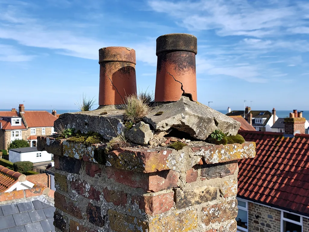 Top of a brick chimney with cracked mortar flaunching around the pots