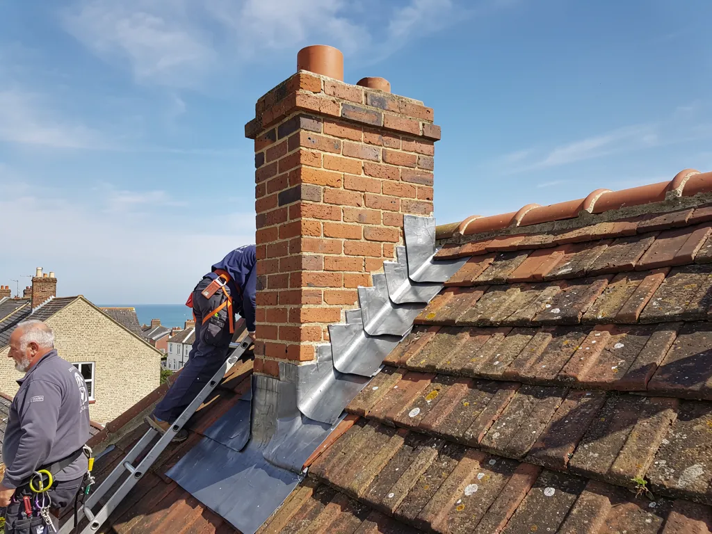 Close-up of new lead step flashing dressed against a red brick chimney on a clay-tiled roof