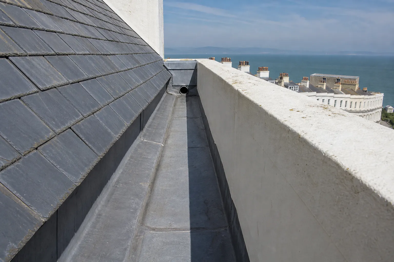 Lead-lined parapet gutter behind a stucco parapet, with grey slates running down to it