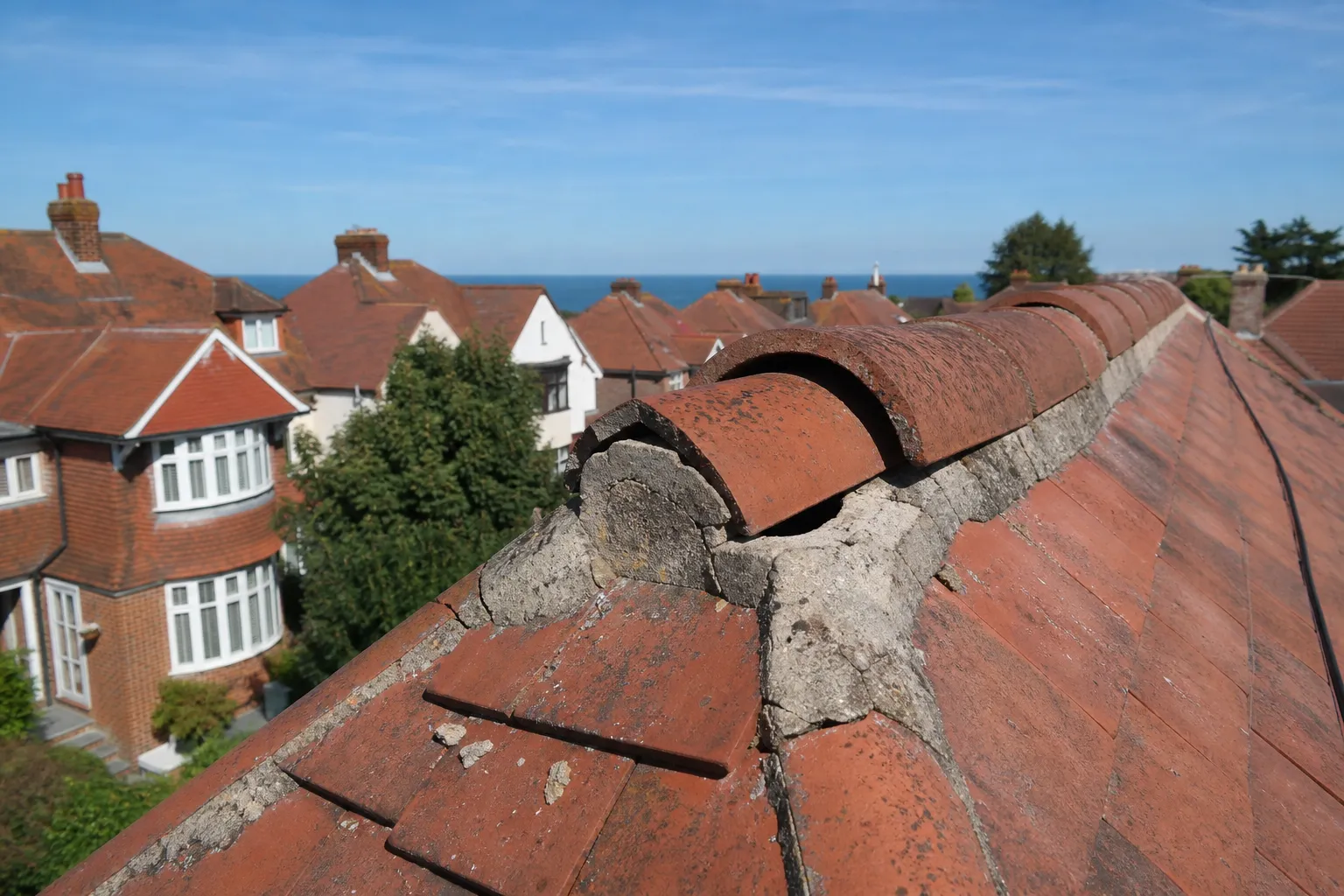 Cracked bedding mortar under the half-round ridge of a clay-tiled semi, the ridge tiles working loose