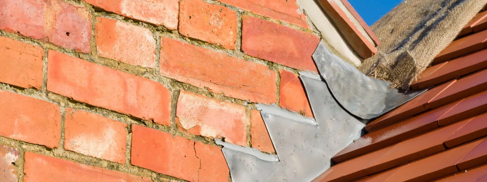 Close-up of lead step flashing against red brick and tiles